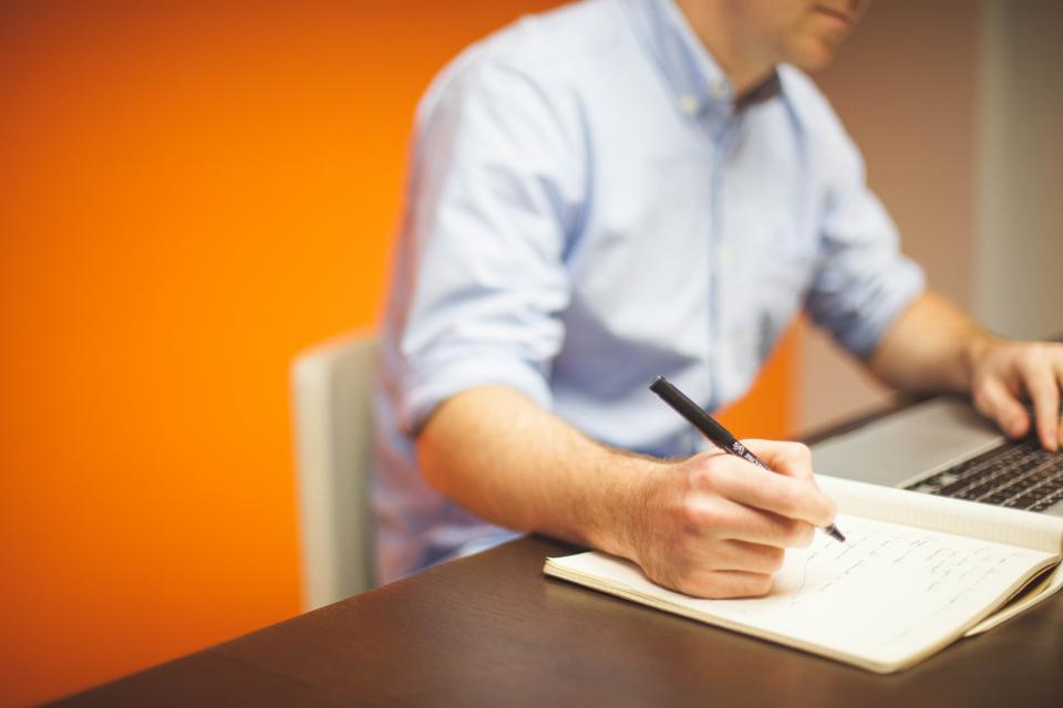 Person taking notes beside a laptop